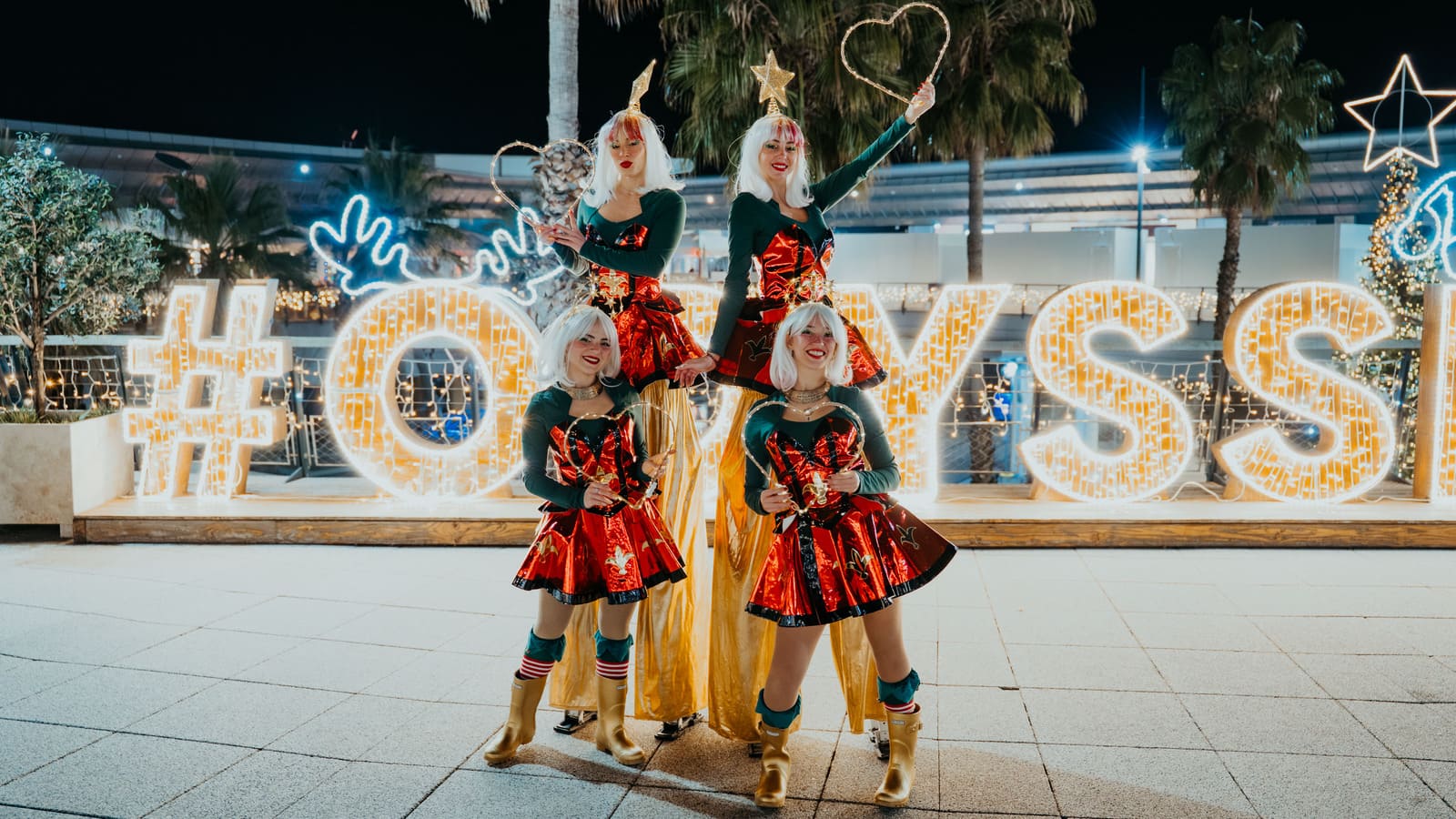 Parade de Noël avec artistes au sol et échassiers en costumes lumineux dans un centre commercial